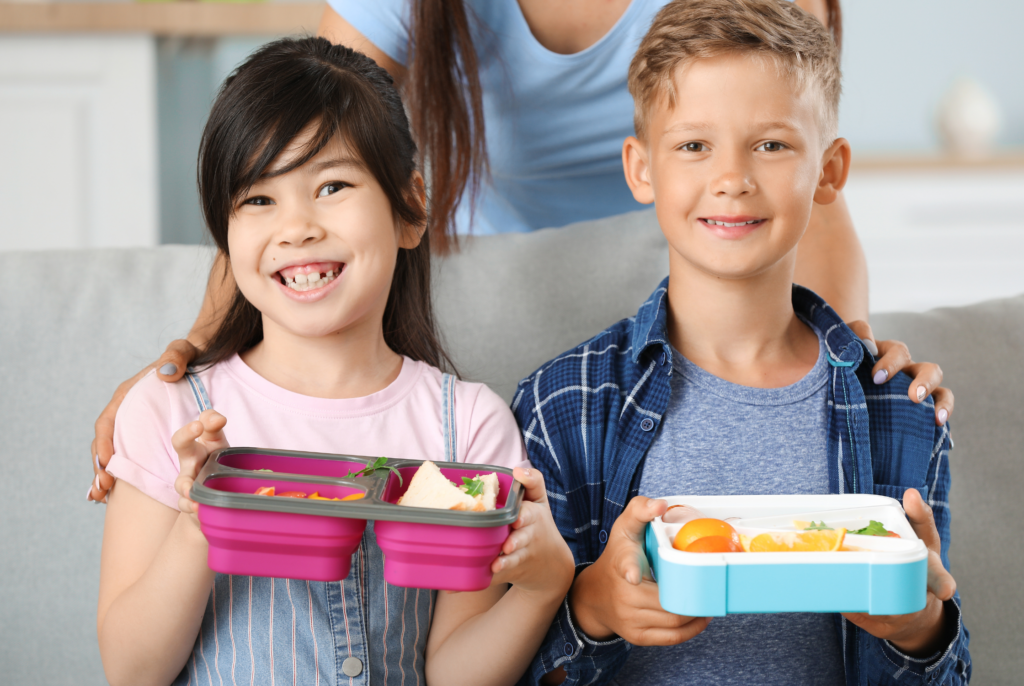 two kids holding bento boxed lunches with smiles