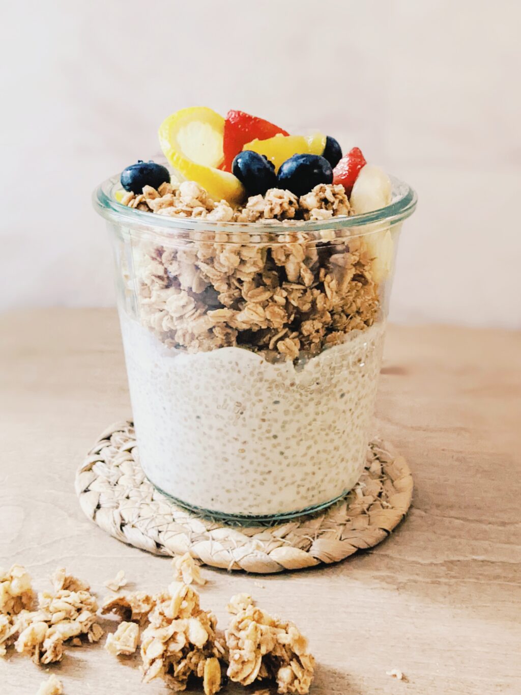 close up of chia pudding in a clear glass jar topped with granola and fresh fruit