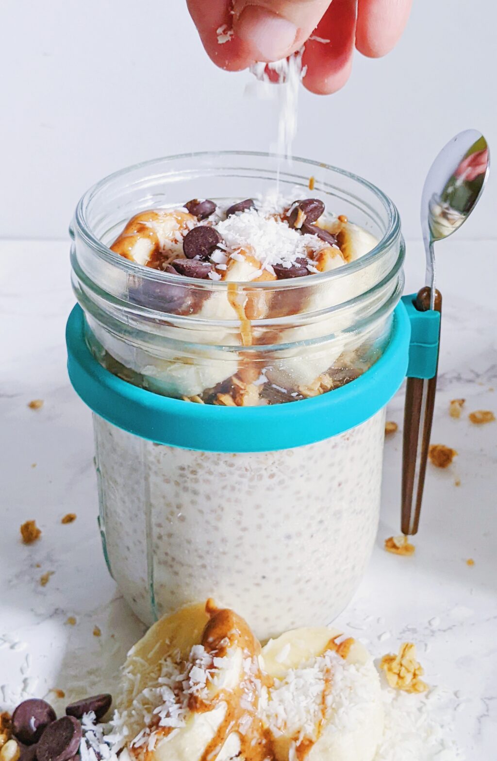 close up of a hand sprinkling coconut shreds on a jar of chia pudding