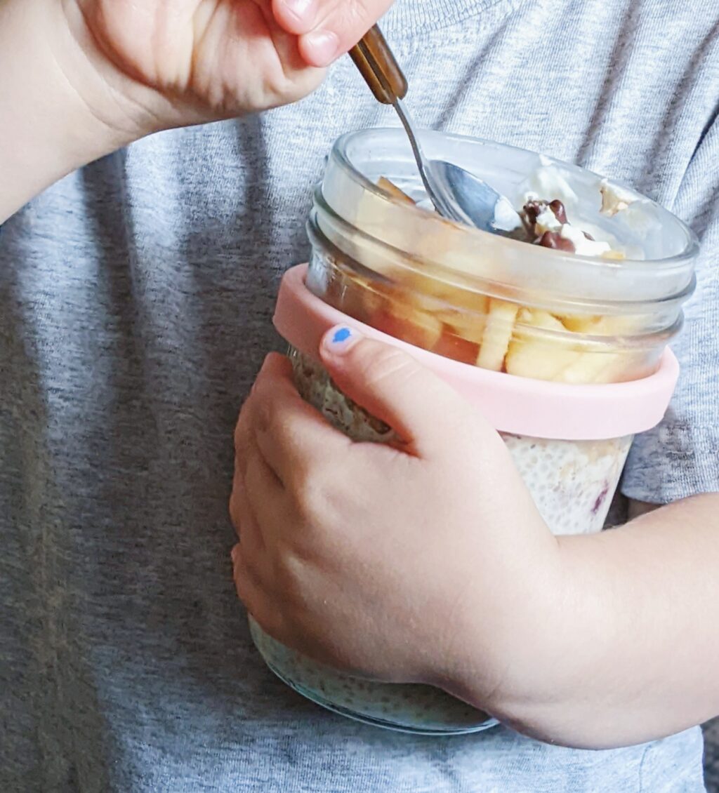 close up of a child's hand holding a jar of chia pudding with a spoon
