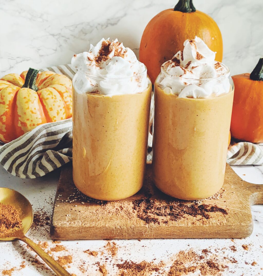 side view of pumpkin pie smoothies in glass mugs topped with whipped cream