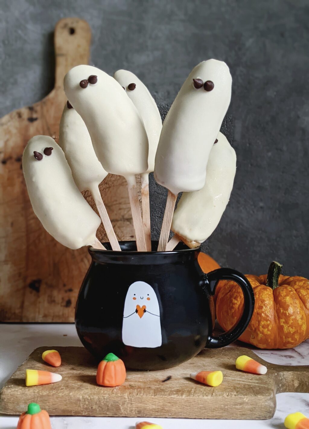 close up of banana pops in a small black bowl surrounded by pumpkins