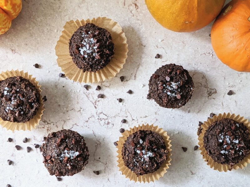 top down view of double chocolate pumpkin muffins on a marble surface with pumpkins in the background