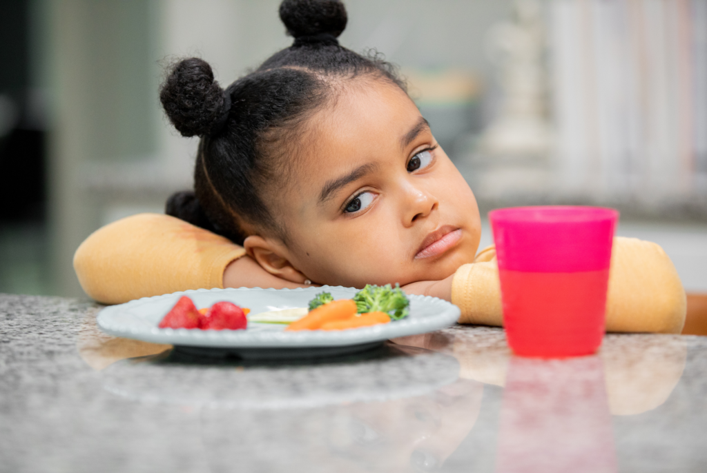 close up of a cute child refusing to eat her dinner with her head down at the table