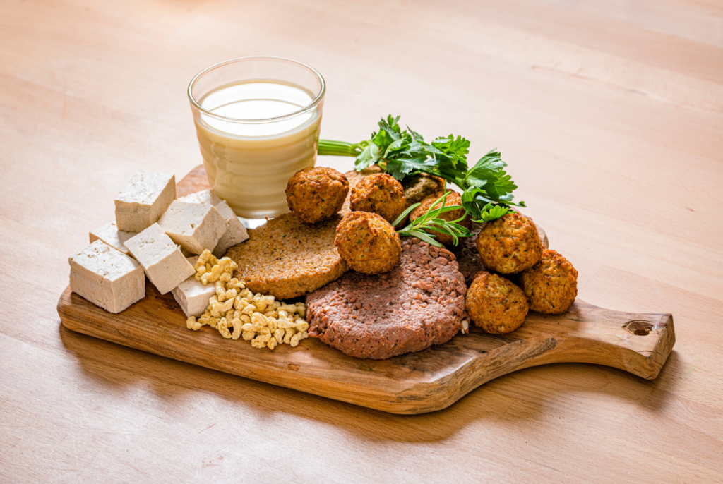 a bunch of plant based foods in a wooden platter including tofu and soy milk
