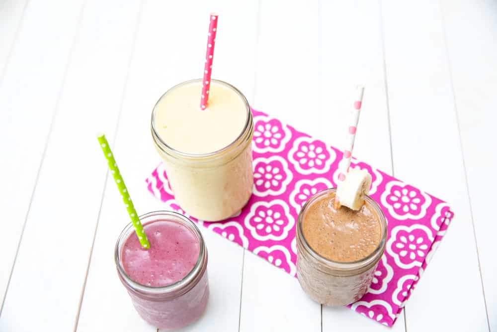 top down view of a variety of smoothies in glass jars with straws
