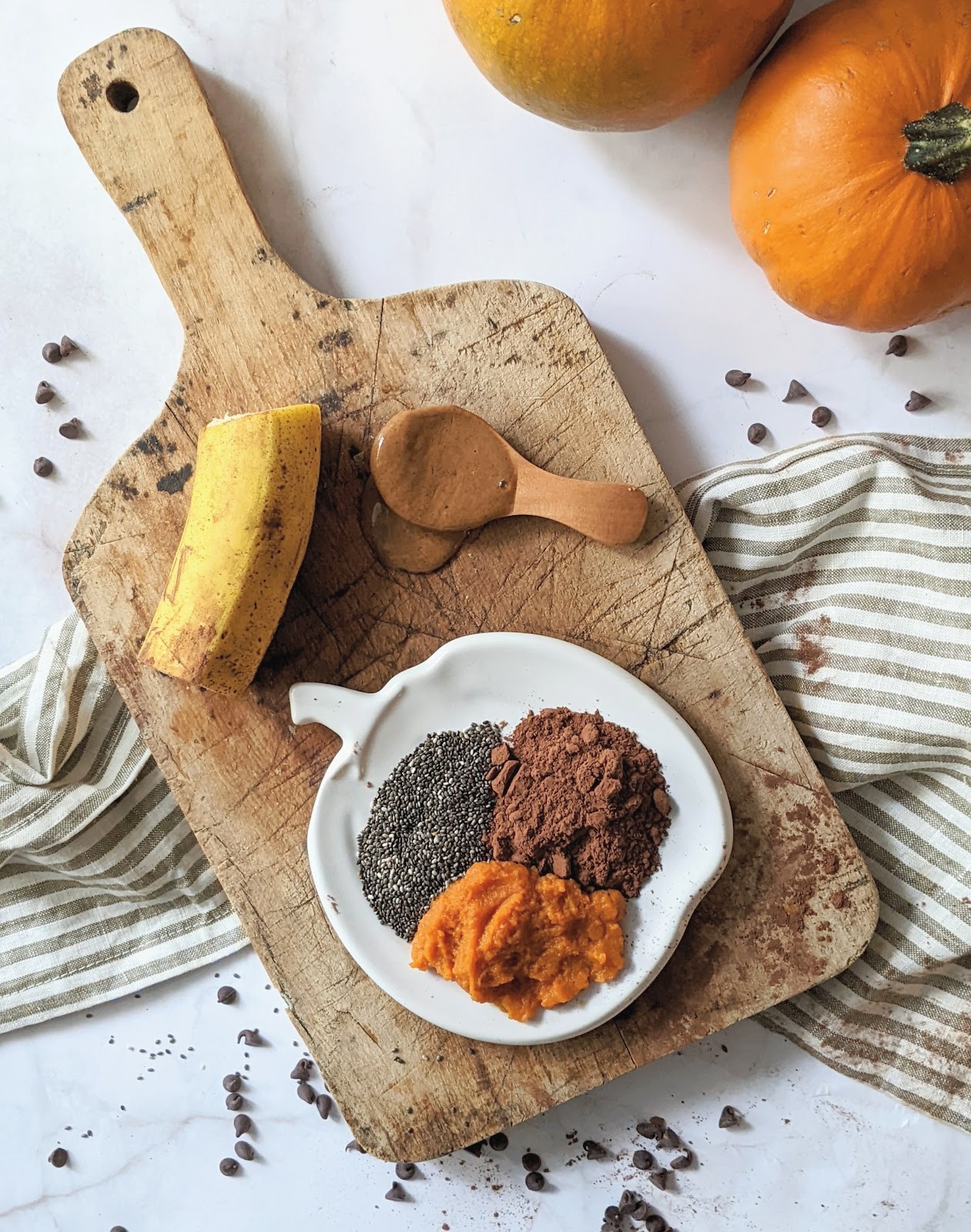 top down view of ingredients needed to make pumpkin muffins including cocoa powder, chocolate chips, pumpkin, nut butter and banana