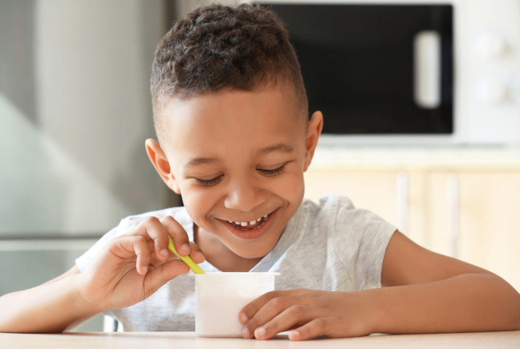 close up of a boy eating yogurt at a table with a spoon