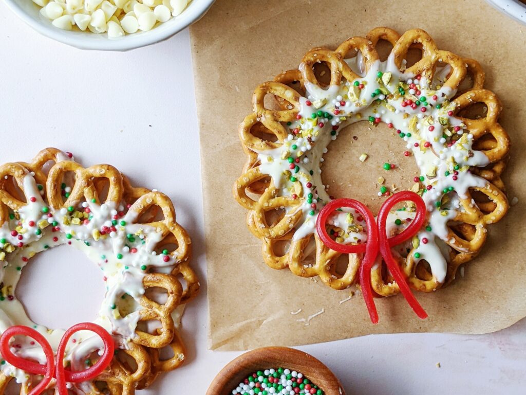 top down view of two chocolate pretzel wreaths side by side with sprinkles and a candy bow on top 