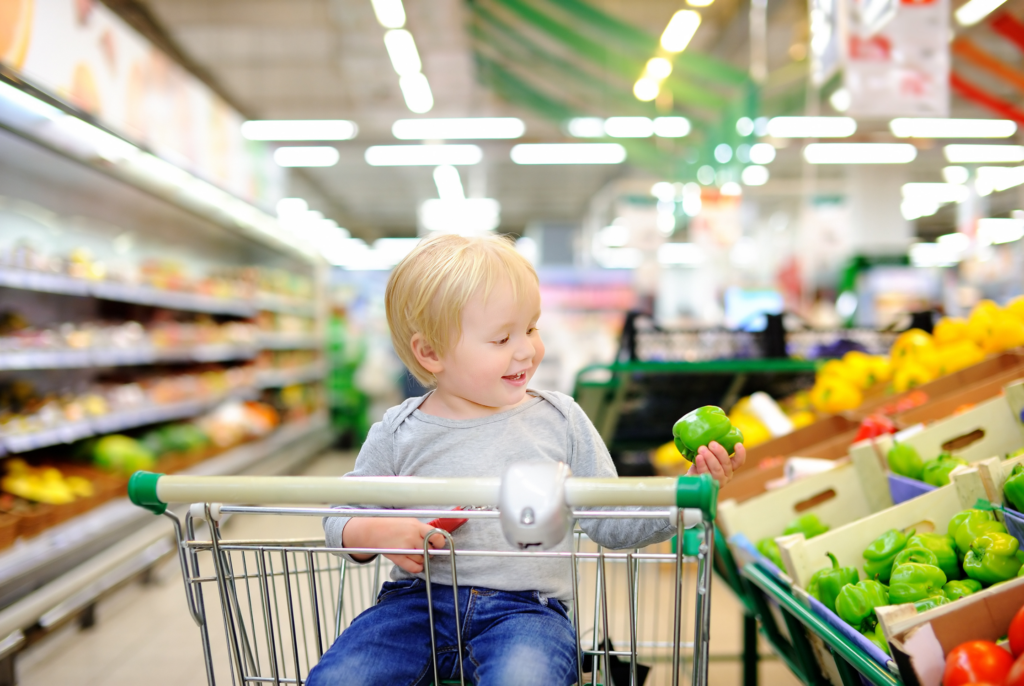 close up of a toddler in a grocery cart holding a green pepper with a smile