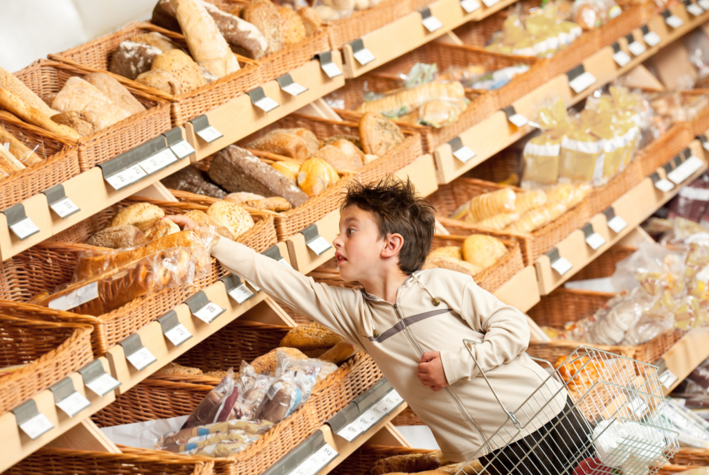 a young boy reaching for a loaf of bread from a large grocery store bakery