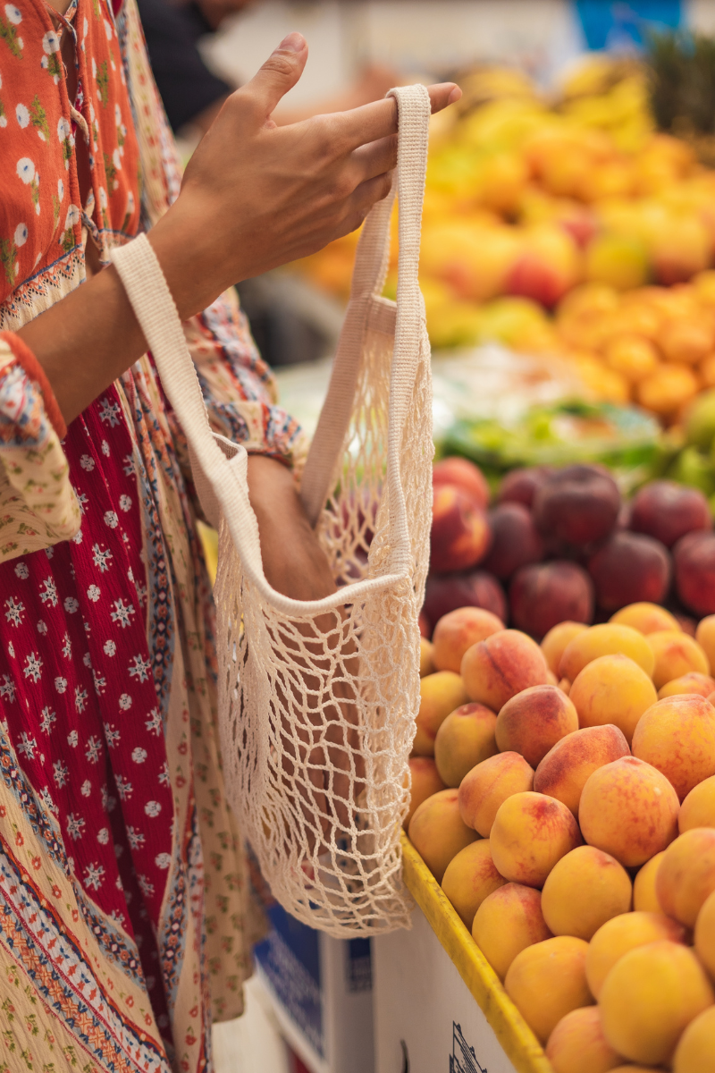 close up of a woman holding a mesh reusable bag when grocery shopping for fruits