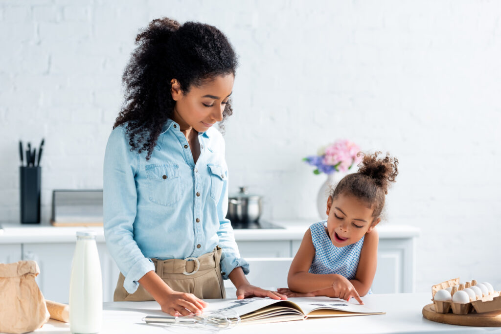 african american mother and daughter looking at cookbook in kitchen