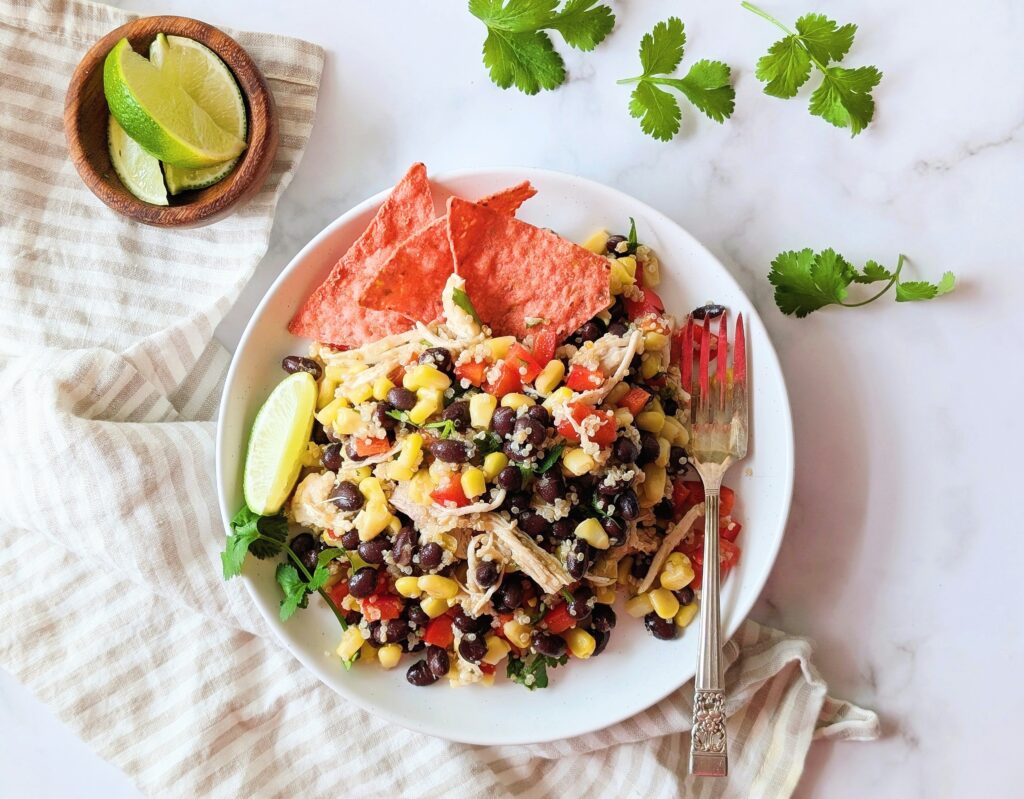 top down view of loaded fiesta salad in a white bowl topped with lime wedge and shredded chicken