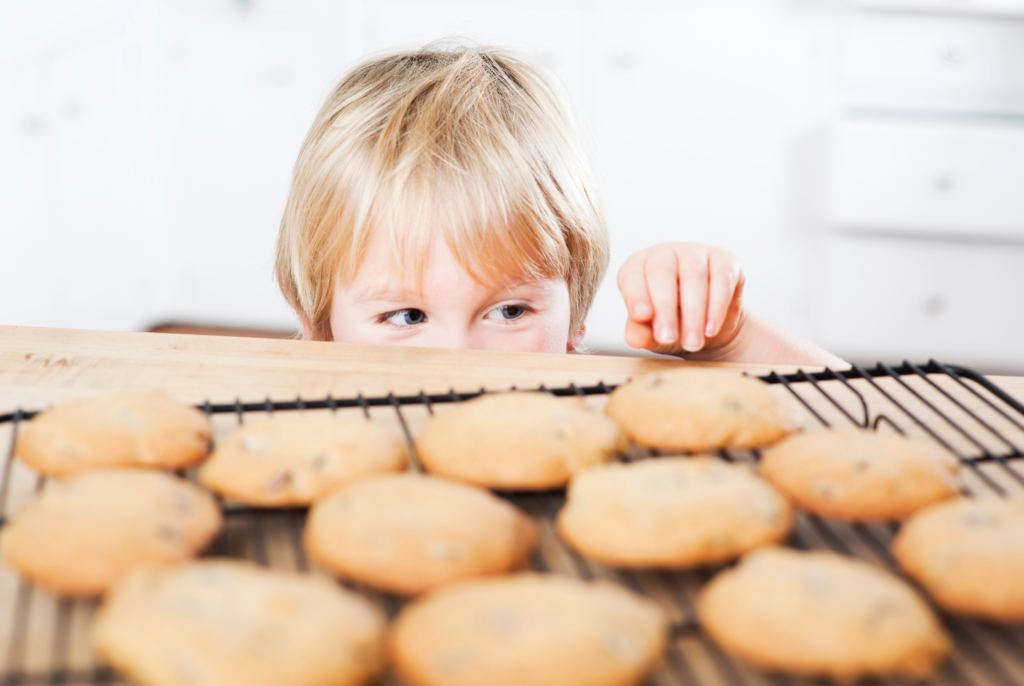 a little boy trying to sneak cookies off the baking rack